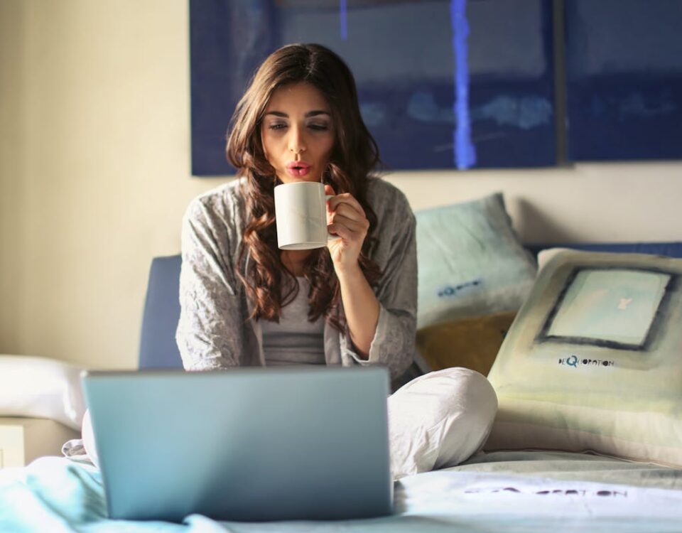 Woman in Grey Jacket Sits on Bed Uses Grey Laptop