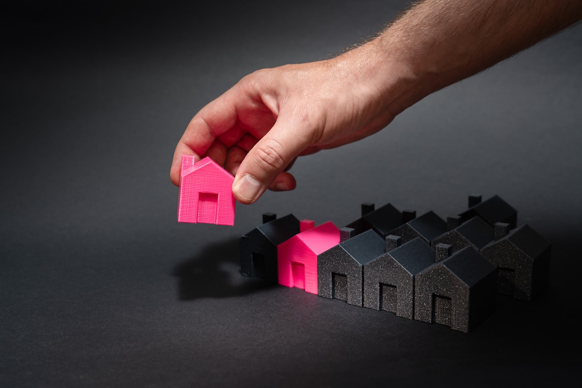 A hand reaching for a pink house in front of a row of houses