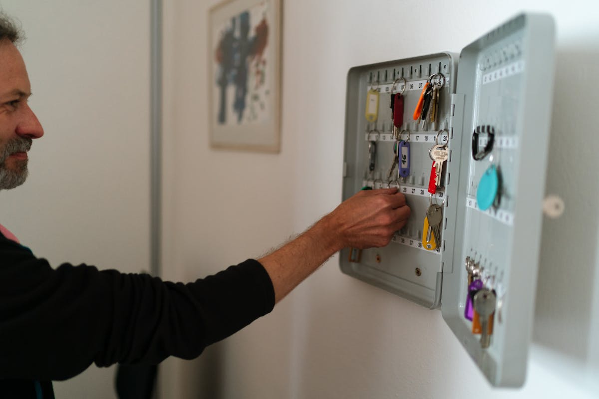 A man arranges keys in a wall-mounted cabinet inside an office setting.