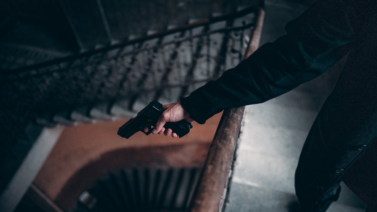 Arm holding a gun on a dimly lit spiral staircase, creating a tense atmosphere.