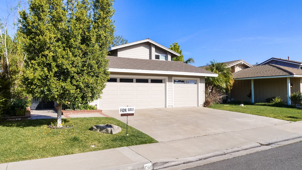 Beautiful suburban house with a for sale sign on a sunny day.