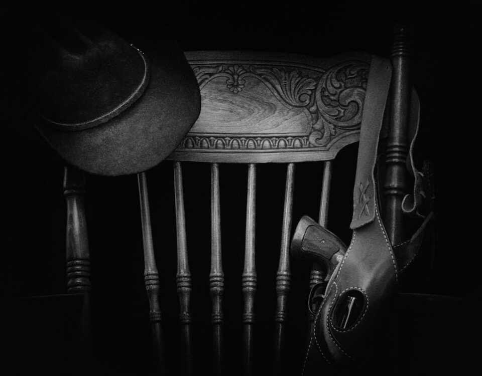 A classic western-themed black and white still life featuring a hat, wooden chair, and gun.