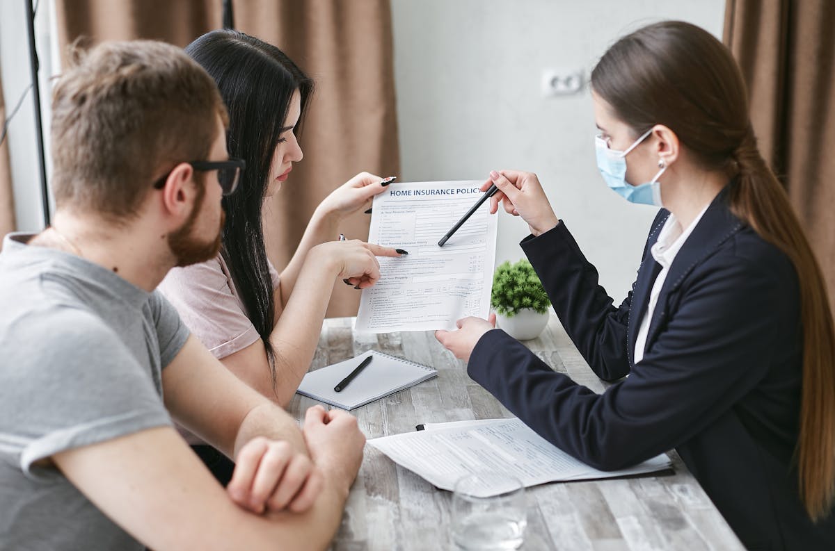 Three adults discuss a home insurance policy at a meeting table indoors.