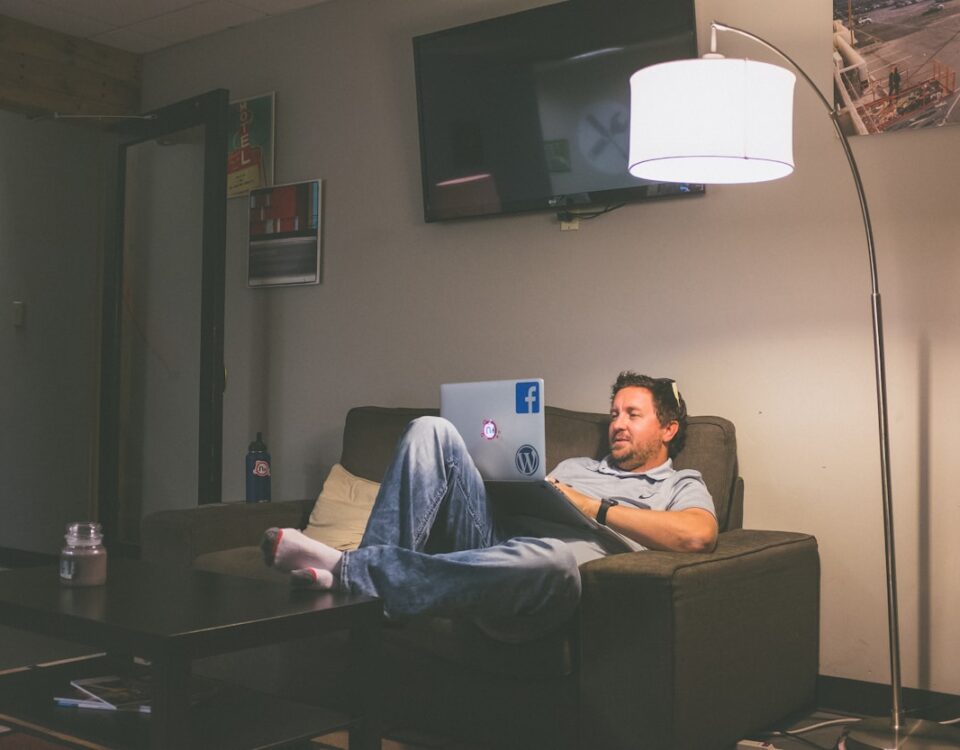 man lying on couch while using laptop computer