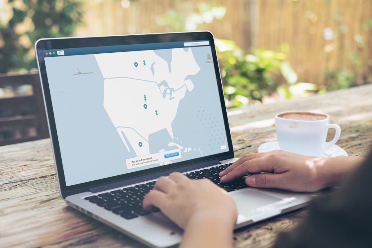 Hands typing on a laptop outdoors with a VPN interface displayed, next to a cup of coffee.