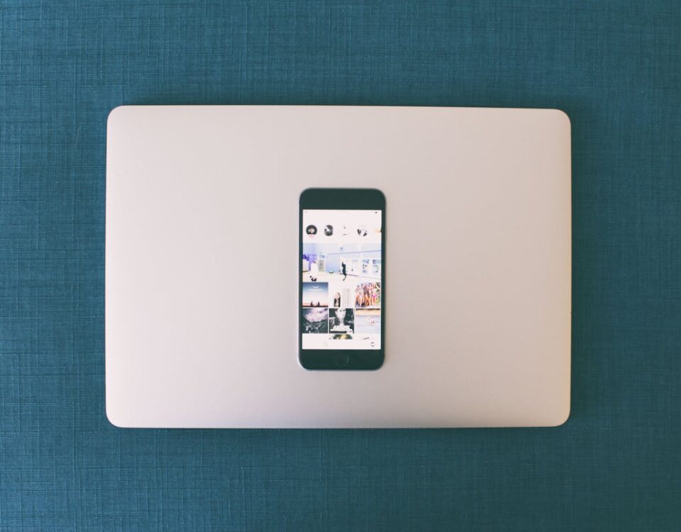 Flat lay of a smartphone on a laptop with social media photos on screen.