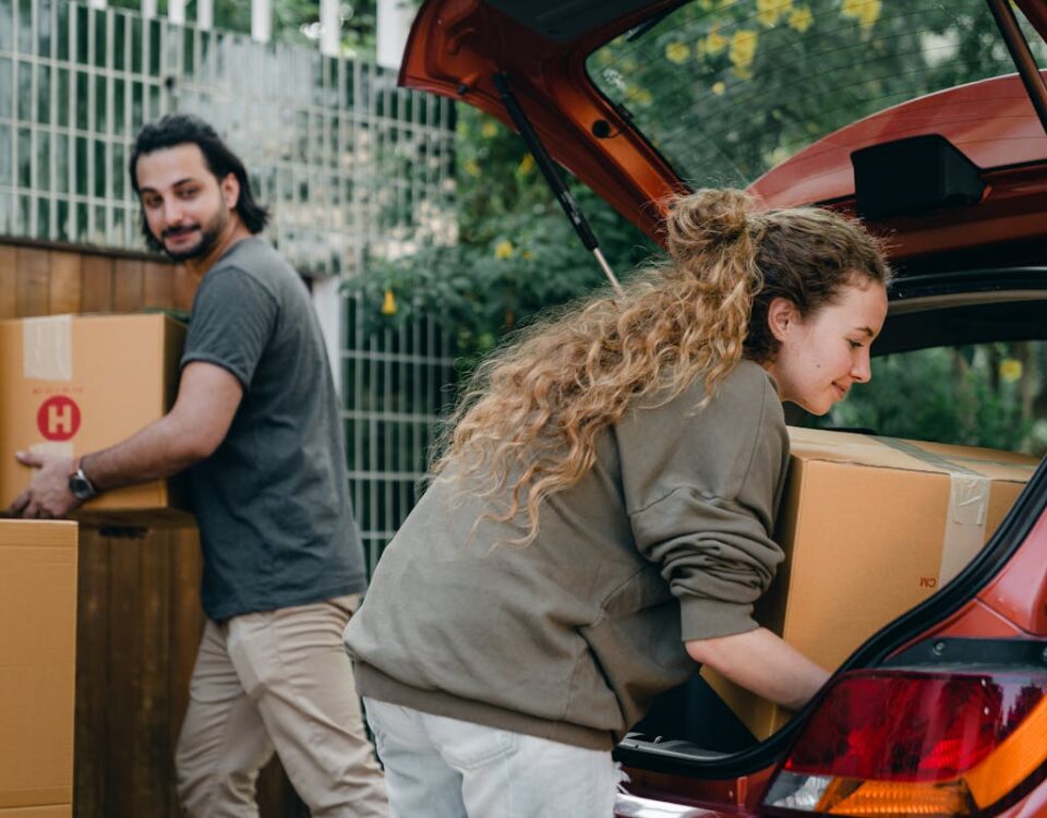 Positive multiethnic boyfriend and girlfriend unloading car trunk during moving to new home in quiet green yard on summer day