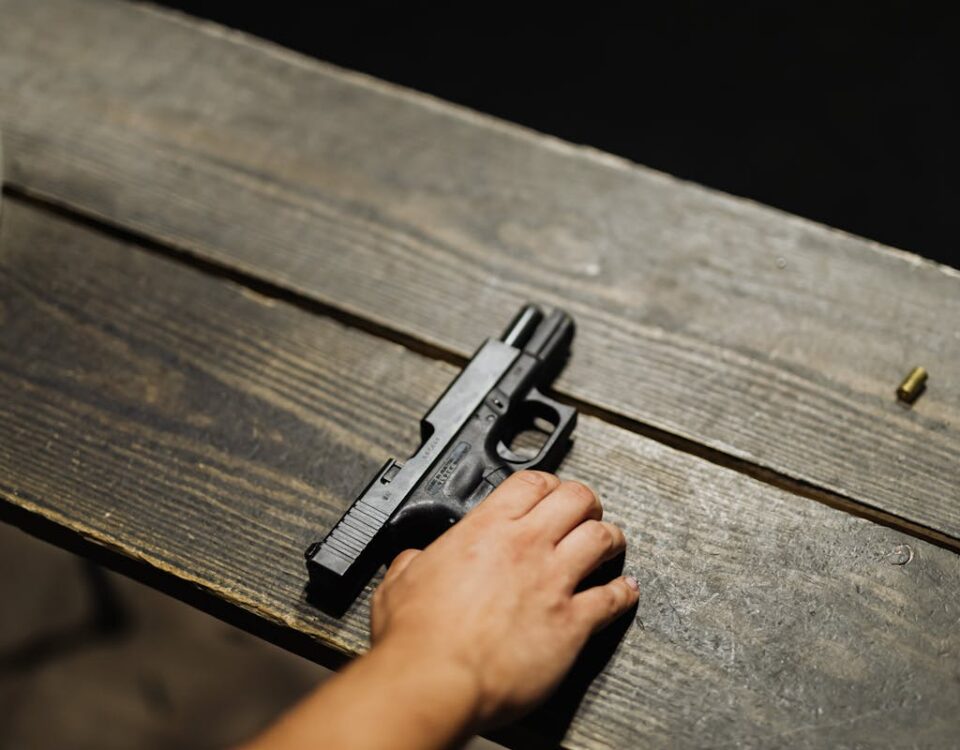 Close-up of a hand holding a handgun on a wooden table with bullet casing.