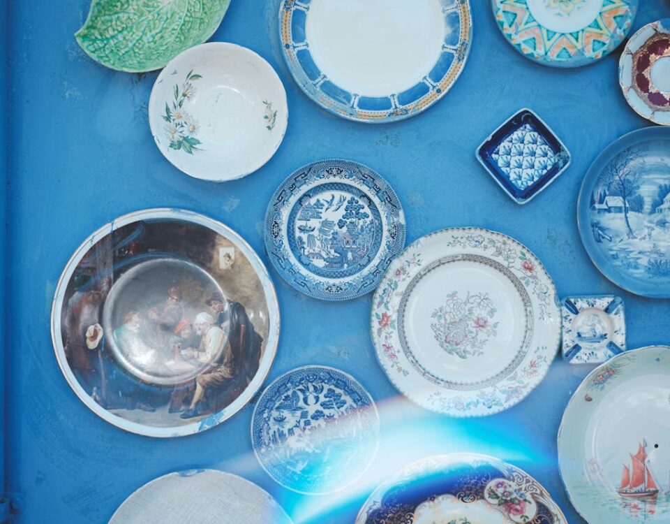 Assorted vintage plates of different sizes and ornaments hanging on bright blue wall in light studio