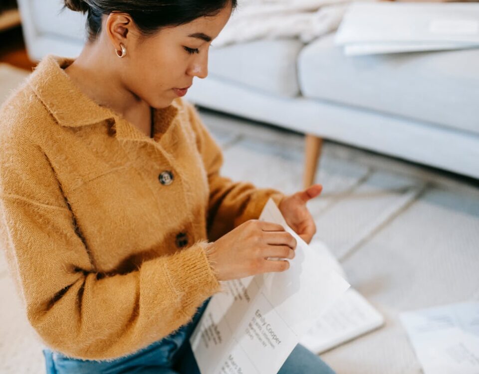 Young woman sitting on the floor reviewing paperwork in a cozy home setting.