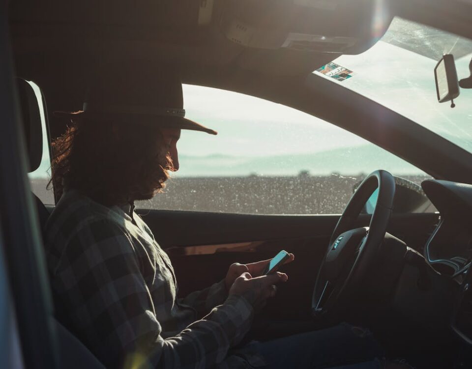 Profile of a man with a hat using a phone inside a car during the day.