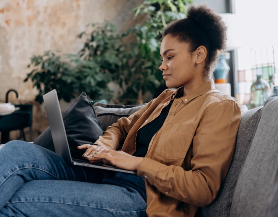 A young woman in casual clothing works on her laptop in a cozy home office setting.