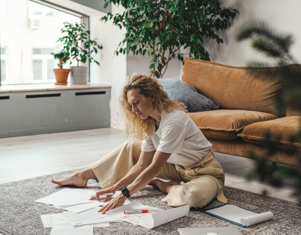 A woman sitting on the floor of her living room working on documents and papers, embodying a comfortable work-from-home atmosphere.