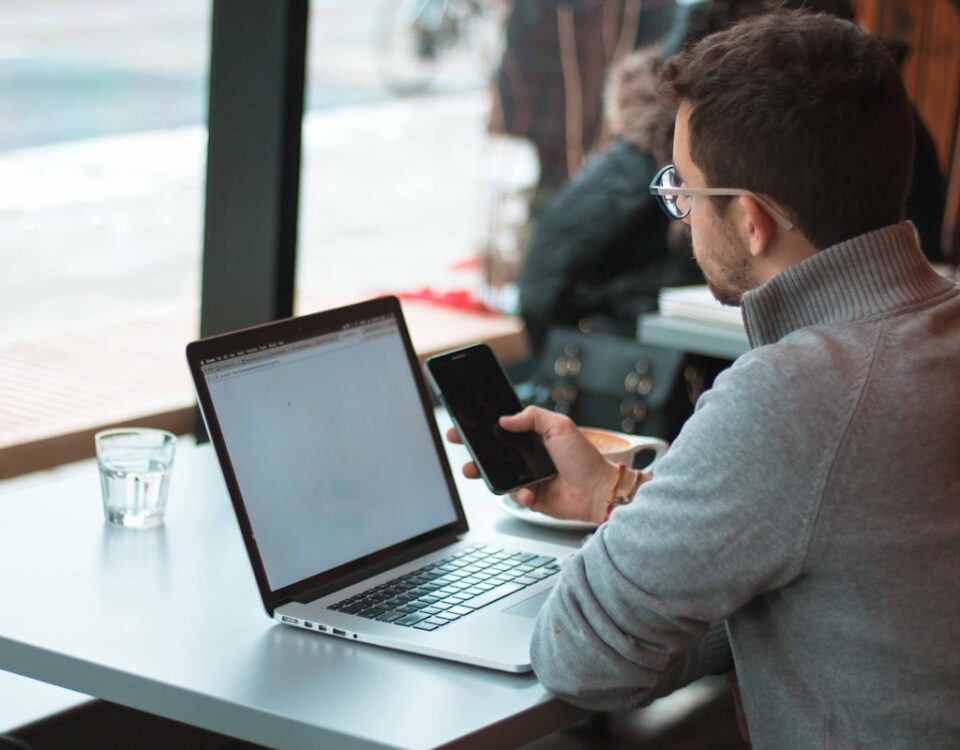 man sitting near table with laptop and smartphone near window