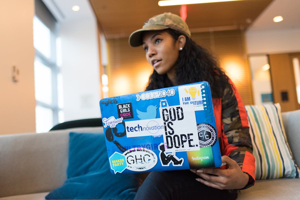 Tech-savvy woman with sticker-decorated laptop working indoors, showing innovation and creativity.