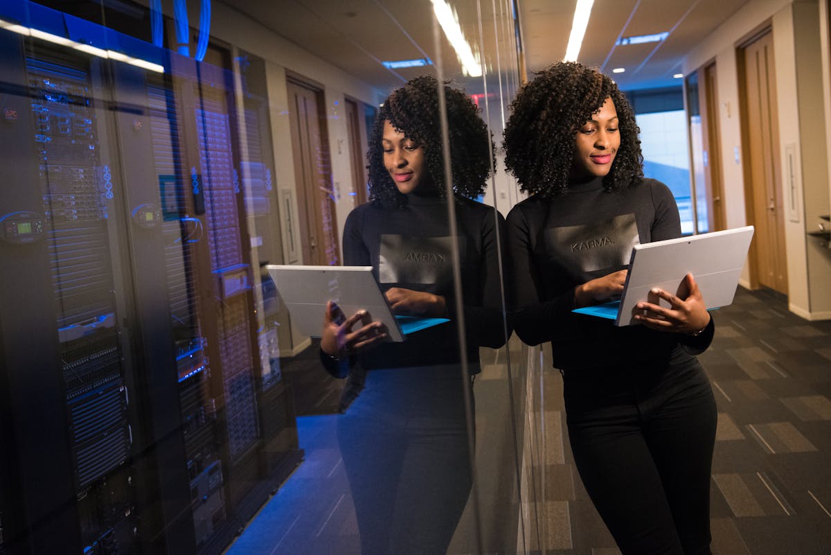 African American woman standing in modern office using laptop, reflecting professionalism and technology engagement.