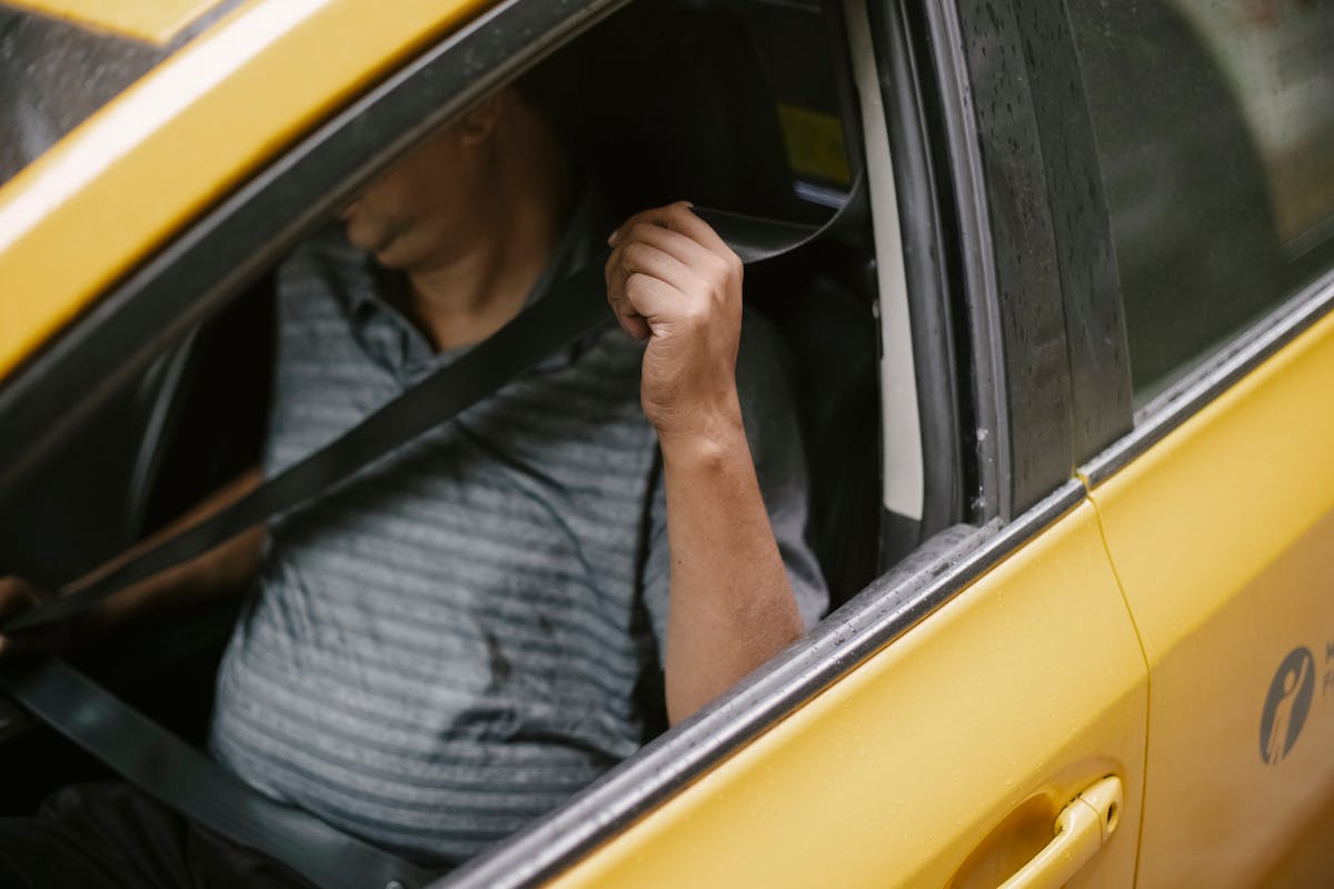 A man securely fastens his seatbelt inside a yellow taxi, emphasizing safety during urban transport.