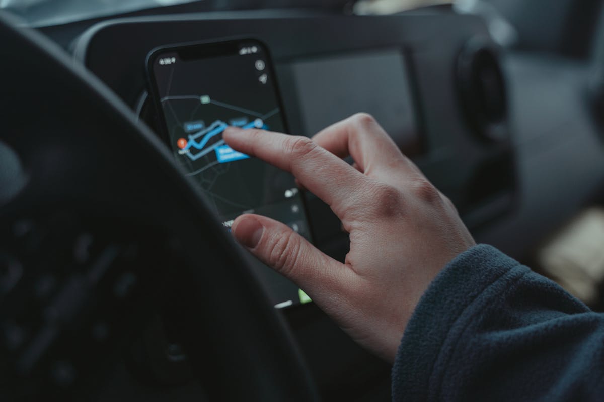 Hand interacting with GPS navigation on a smartphone mounted in a car interior.