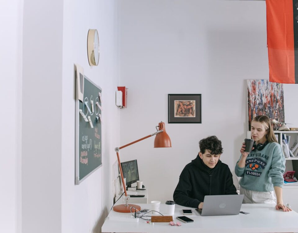 Two young adults working in a modern office, collaborating on a project with a laptop.