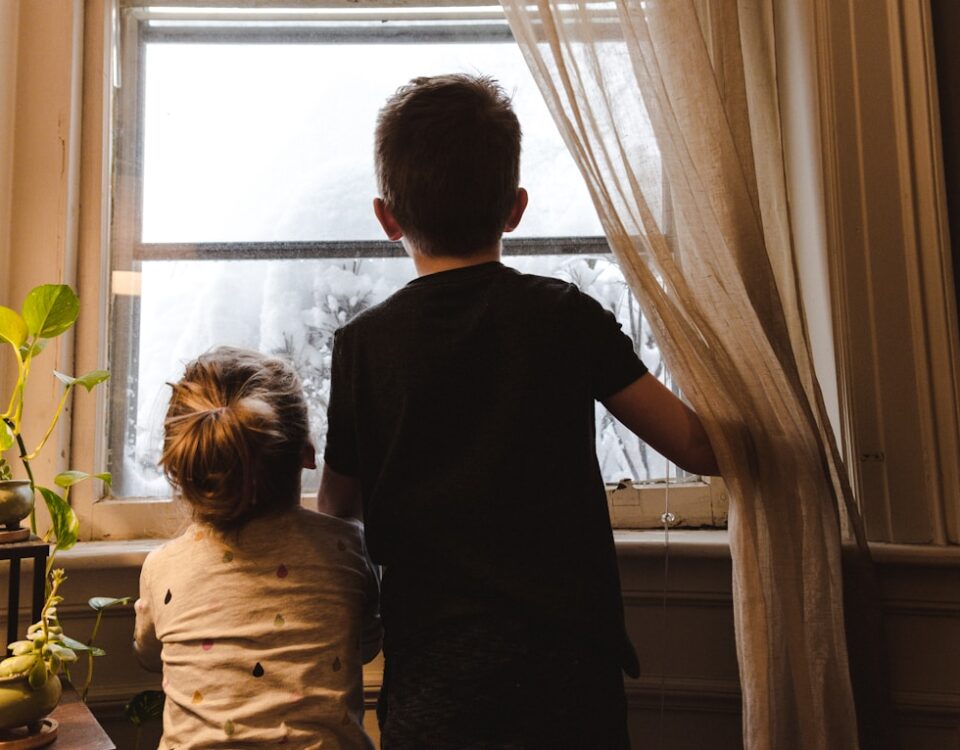 boy and girl standing near window looking outside